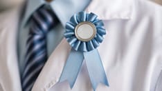photo of blue award ribbon pinned to the lapel next to a striped necktie