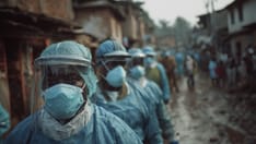 photo of A line of healthcare workers wearing blue protective suits, masks, and face shields walks down a muddy outdoor stree