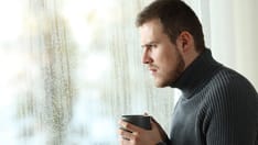 photo of Angry man looking out of a window on a rainy day. Side view portrait of an angry man looking out of a window on a ra