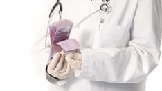 photo of Doctor counting a wad of money. Cropped torso view of a doctor's gloved hands wearing a labcoat counting a wad of 50