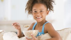 photo of Young girl eats cereal in the living room, smiling at the camera
