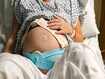 An unrecognisable mature pregnant woman lies on a hospital delivery bed as she has fetal monitoring. Cardiotocography is usually called a 'CTG' by medical staff. It can be used to monitor a baby's heart rate and a mother's contractions during pregnancy