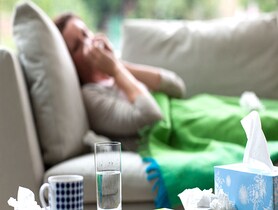 photo of Sick woman laying on sofa blowing nose